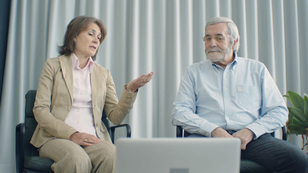An older couple talking with a clinician over a laptop video call at home